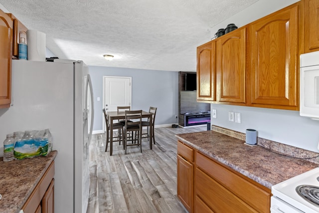 kitchen with brown cabinetry, a textured ceiling, baseboards, light wood finished floors, and white appliances