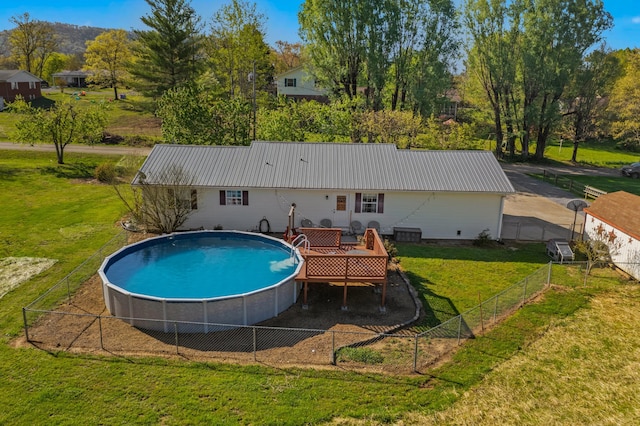 rear view of property featuring a lawn, an outdoor pool, metal roof, and fence