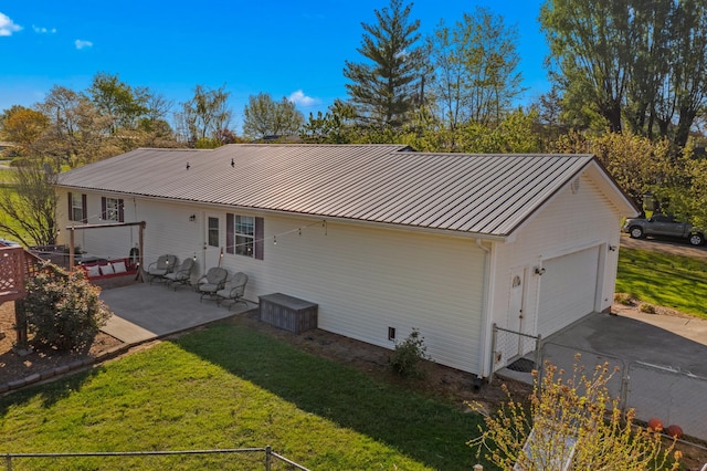 back of house featuring a patio area, aphalt driveway, an attached garage, a yard, and metal roof