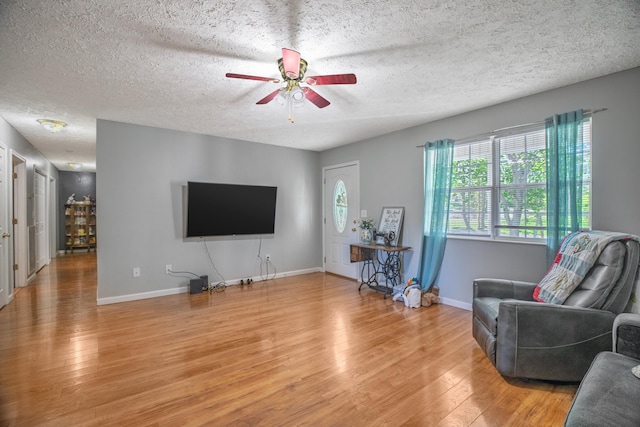 living room featuring light wood finished floors, a ceiling fan, baseboards, and a textured ceiling