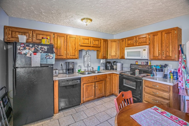 kitchen with a sink, black appliances, brown cabinets, light tile patterned floors, and light countertops