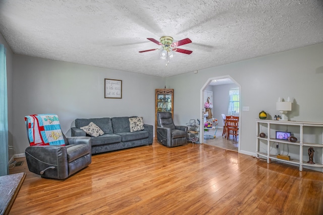 living area with wood finished floors, a textured ceiling, ceiling fan, arched walkways, and baseboards