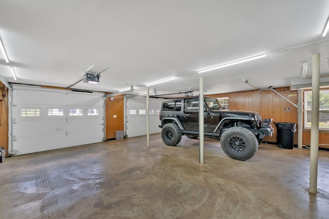 garage with wood walls, a garage door opener, and a carport