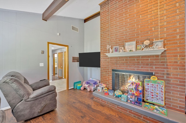 living room with hardwood / wood-style floors, beam ceiling, and a brick fireplace