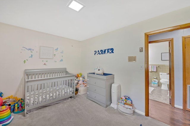 carpeted bedroom featuring ensuite bathroom and a crib