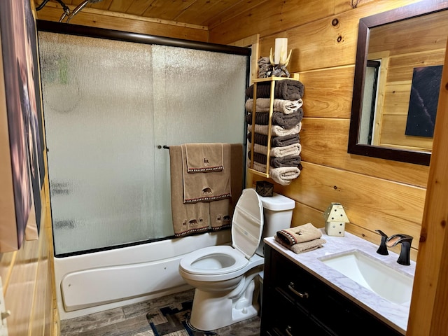 full bathroom with wood walls, toilet, vanity, and combined bath / shower with glass door