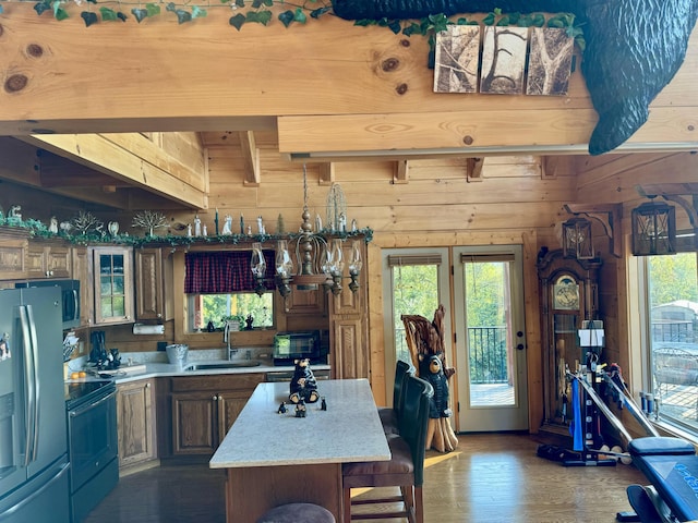 kitchen with electric range, a center island, sink, stainless steel refrigerator with ice dispenser, and wooden walls