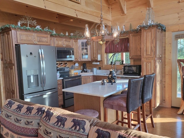 kitchen featuring sink, stainless steel appliances, decorative light fixtures, wooden walls, and light wood-type flooring