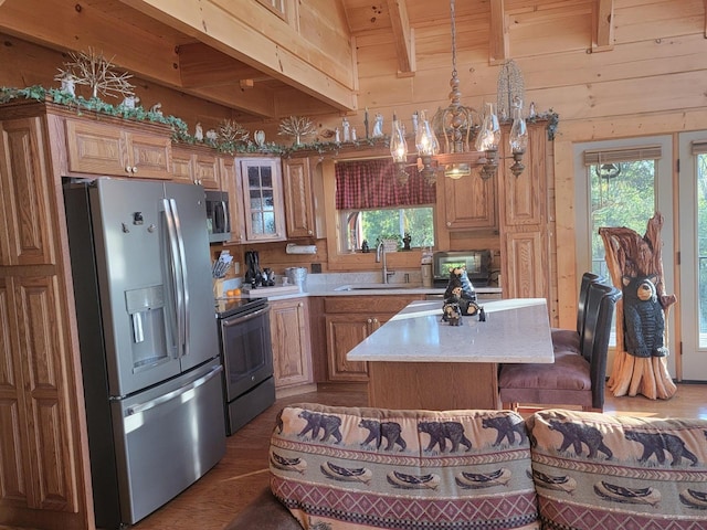 kitchen with stainless steel appliances, sink, a kitchen island, hanging light fixtures, and wood walls