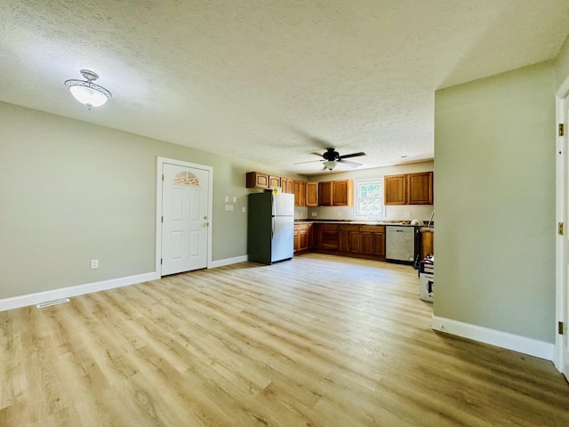 unfurnished living room featuring ceiling fan, sink, a textured ceiling, and light hardwood / wood-style flooring