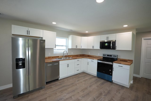 kitchen featuring white cabinetry, butcher block counters, stainless steel appliances, a sink, and wood finished floors