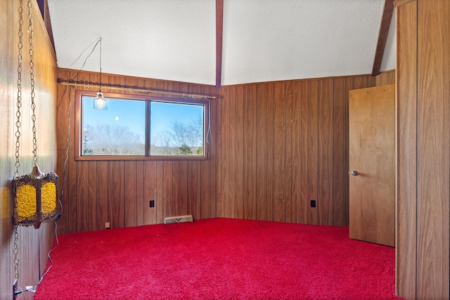 spare room with vaulted ceiling, carpet, and wood walls