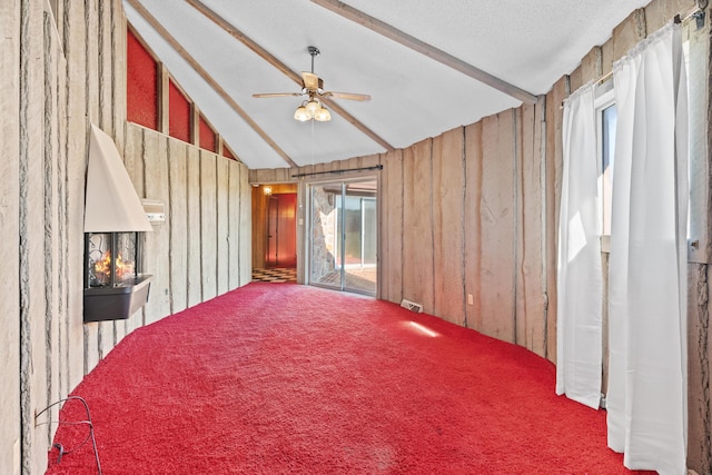 empty room with lofted ceiling with beams, a healthy amount of sunlight, and wood walls