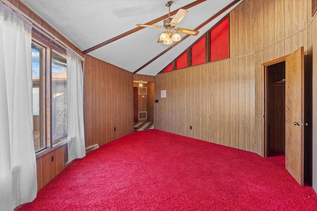 carpeted spare room featuring vaulted ceiling, ceiling fan, and wood walls