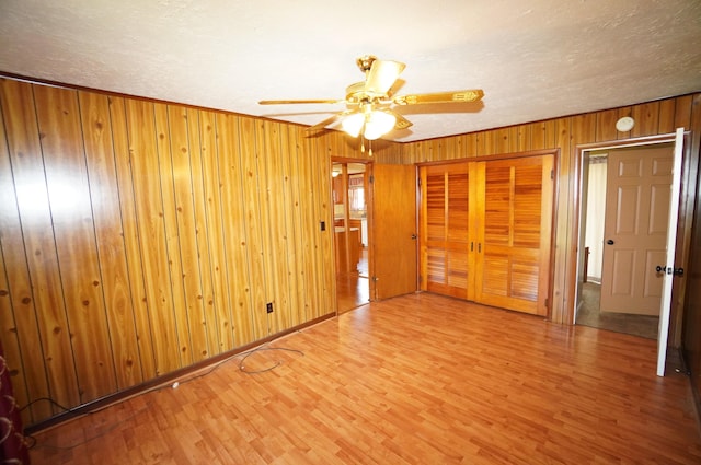 unfurnished bedroom with wooden walls, baseboards, ceiling fan, wood finished floors, and a closet