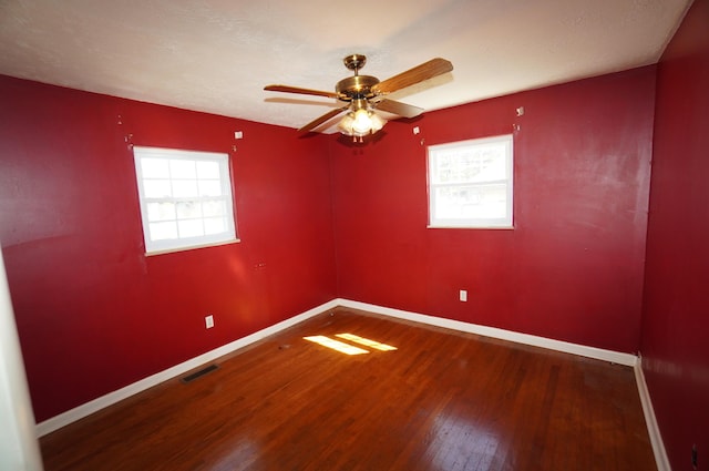 empty room featuring visible vents, wood finished floors, baseboards, and a wealth of natural light