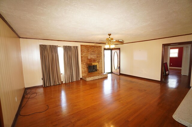 unfurnished living room featuring ornamental molding, a brick fireplace, a textured ceiling, and wood finished floors