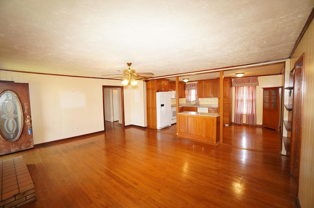 unfurnished living room with a textured ceiling, crown molding, baseboards, ceiling fan, and dark wood-style flooring