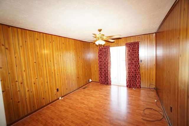 spare room featuring a ceiling fan, light wood-type flooring, wood walls, and baseboards