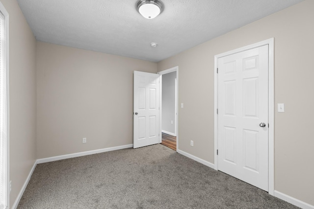 unfurnished bedroom with carpet floors, a textured ceiling, and baseboards