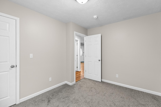 unfurnished bedroom with carpet floors, a textured ceiling, and baseboards