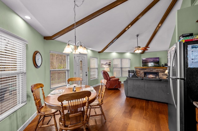 dining space with a wealth of natural light, vaulted ceiling with beams, wood-type flooring, a fireplace, and ceiling fan with notable chandelier