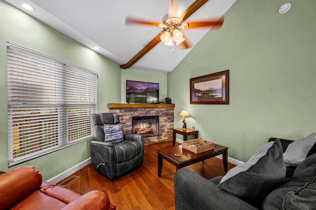 living room with vaulted ceiling with beams, hardwood / wood-style flooring, a stone fireplace, and ceiling fan