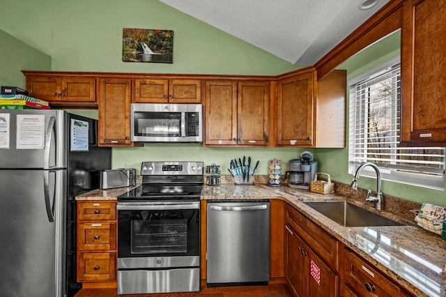 kitchen featuring appliances with stainless steel finishes, light stone counters, lofted ceiling, and sink