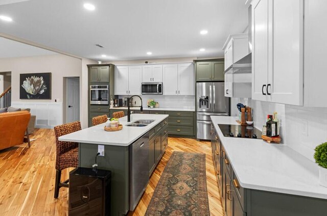 kitchen with a sink, backsplash, a breakfast bar area, appliances with stainless steel finishes, and light wood-type flooring