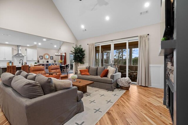 living room featuring high vaulted ceiling, visible vents, light wood-style flooring, a fireplace, and ceiling fan with notable chandelier