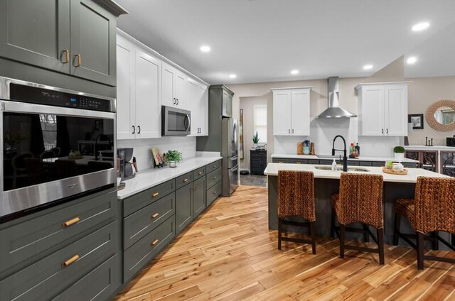 kitchen with light countertops, a breakfast bar, wall chimney exhaust hood, appliances with stainless steel finishes, and a sink