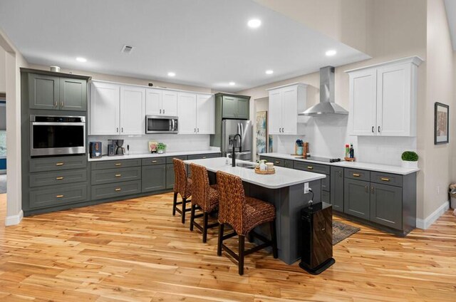 kitchen with a kitchen breakfast bar, light countertops, stainless steel appliances, light wood finished floors, and wall chimney exhaust hood