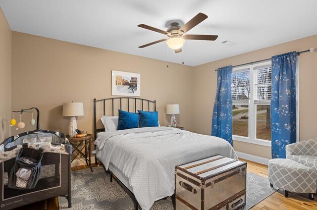 bedroom featuring a ceiling fan, visible vents, baseboards, and wood finished floors