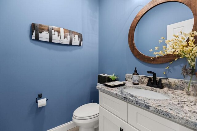 half bathroom featuring baseboards, toilet, and vanity