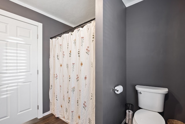 bathroom featuring curtained shower, toilet, wood finished floors, and a textured ceiling