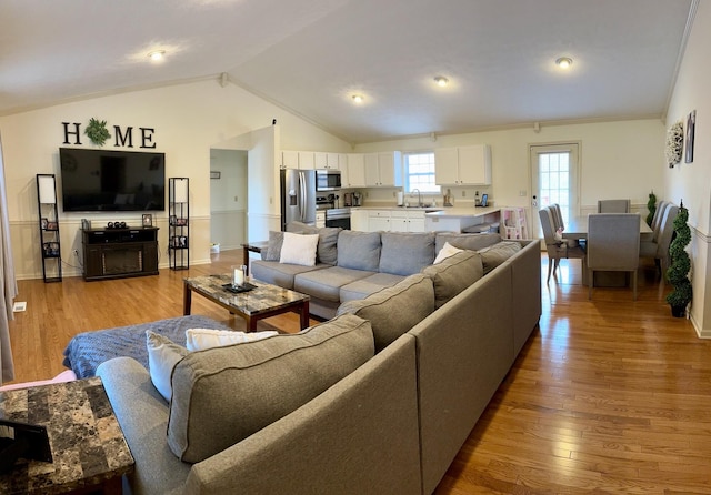 living room with ornamental molding, light hardwood / wood-style floors, lofted ceiling, and sink