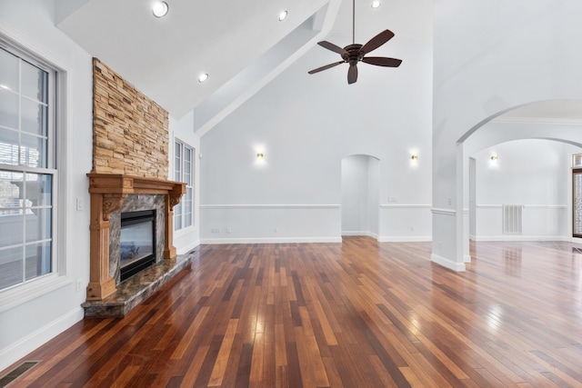 unfurnished living room with high vaulted ceiling, ceiling fan, a stone fireplace, and dark wood-type flooring