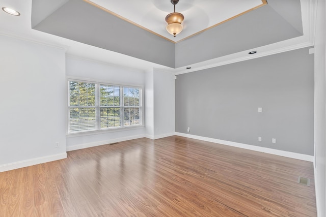 spare room with crown molding, light hardwood / wood-style floors, and a raised ceiling