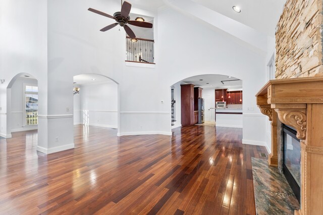 unfurnished living room with ceiling fan with notable chandelier, a large fireplace, dark hardwood / wood-style flooring, and a towering ceiling