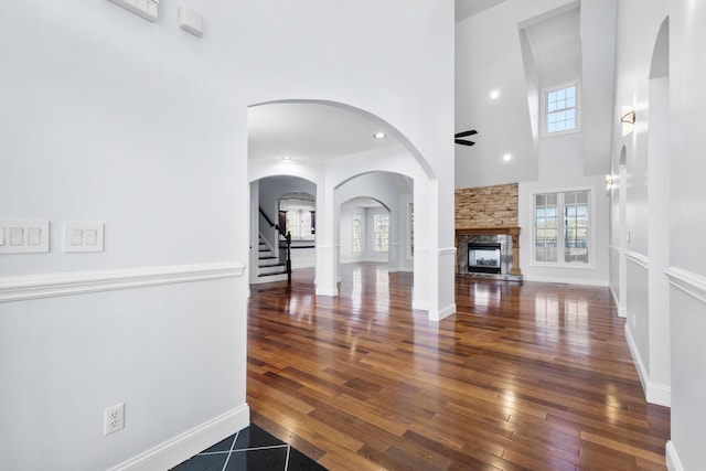 unfurnished living room with dark wood-type flooring, ceiling fan, a fireplace, and a high ceiling