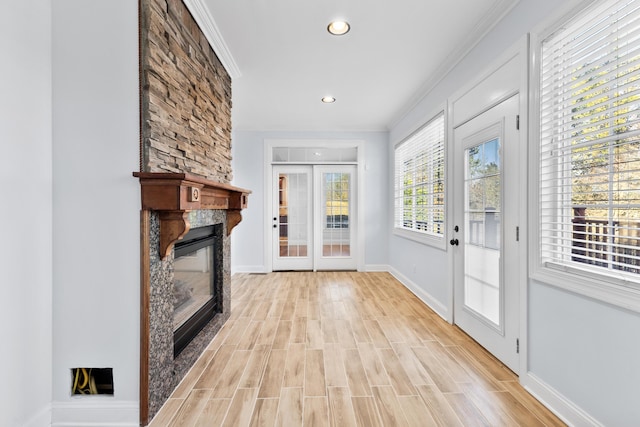 unfurnished living room with crown molding, a fireplace, french doors, and light hardwood / wood-style floors