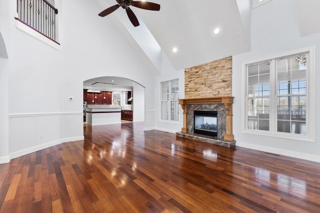 unfurnished living room featuring a fireplace, ceiling fan, a towering ceiling, and dark hardwood / wood-style flooring