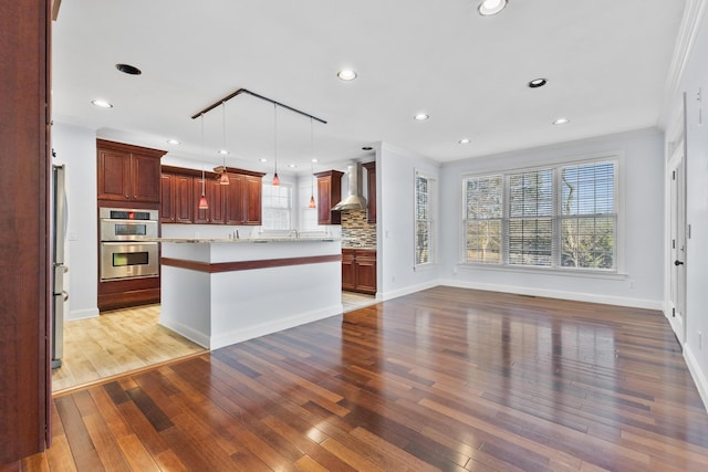 kitchen with pendant lighting, wall chimney range hood, stainless steel appliances, tasteful backsplash, and ornamental molding