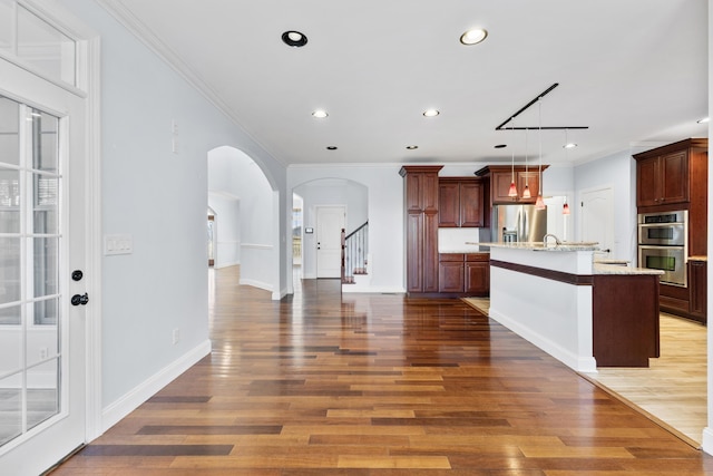 kitchen featuring decorative light fixtures, crown molding, appliances with stainless steel finishes, and a kitchen island with sink