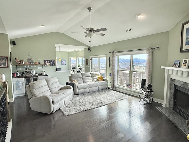 living room featuring vaulted ceiling, bar, dark wood finished floors, a high end fireplace, and a ceiling fan