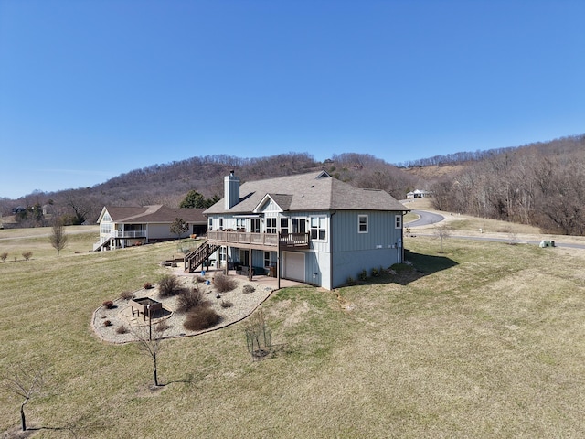 rear view of property featuring stairway, a chimney, a wooden deck, a garage, and a yard