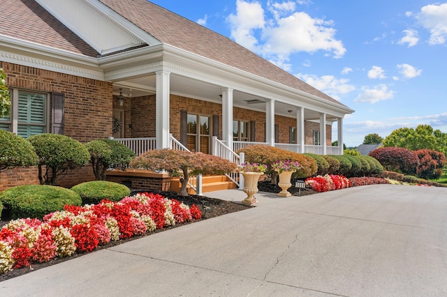 view of exterior entry featuring brick siding, a shingled roof, and a porch