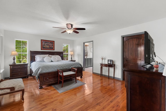 bedroom with connected bathroom, light wood-style floors, baseboards, and a ceiling fan