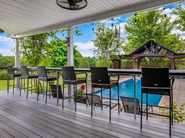deck with outdoor dry bar, a gazebo, a ceiling fan, and an outdoor pool