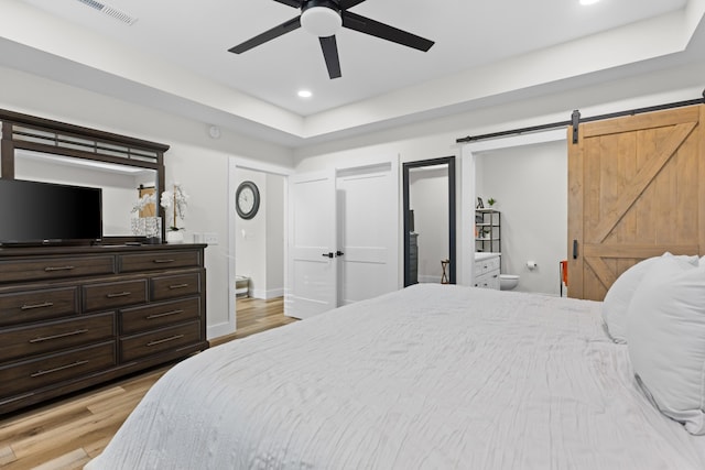 bedroom featuring ceiling fan, a barn door, light wood-type flooring, and ensuite bathroom